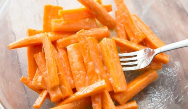 Кусочки моркови в растопленном сливочном масле и металлическая вилка